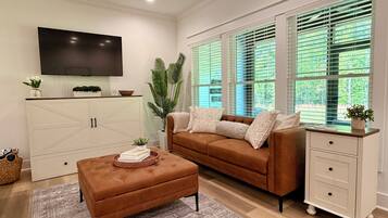 A living room with a brown sofa, a white cabinet, a flat-screen TV, and a large window with blinds.