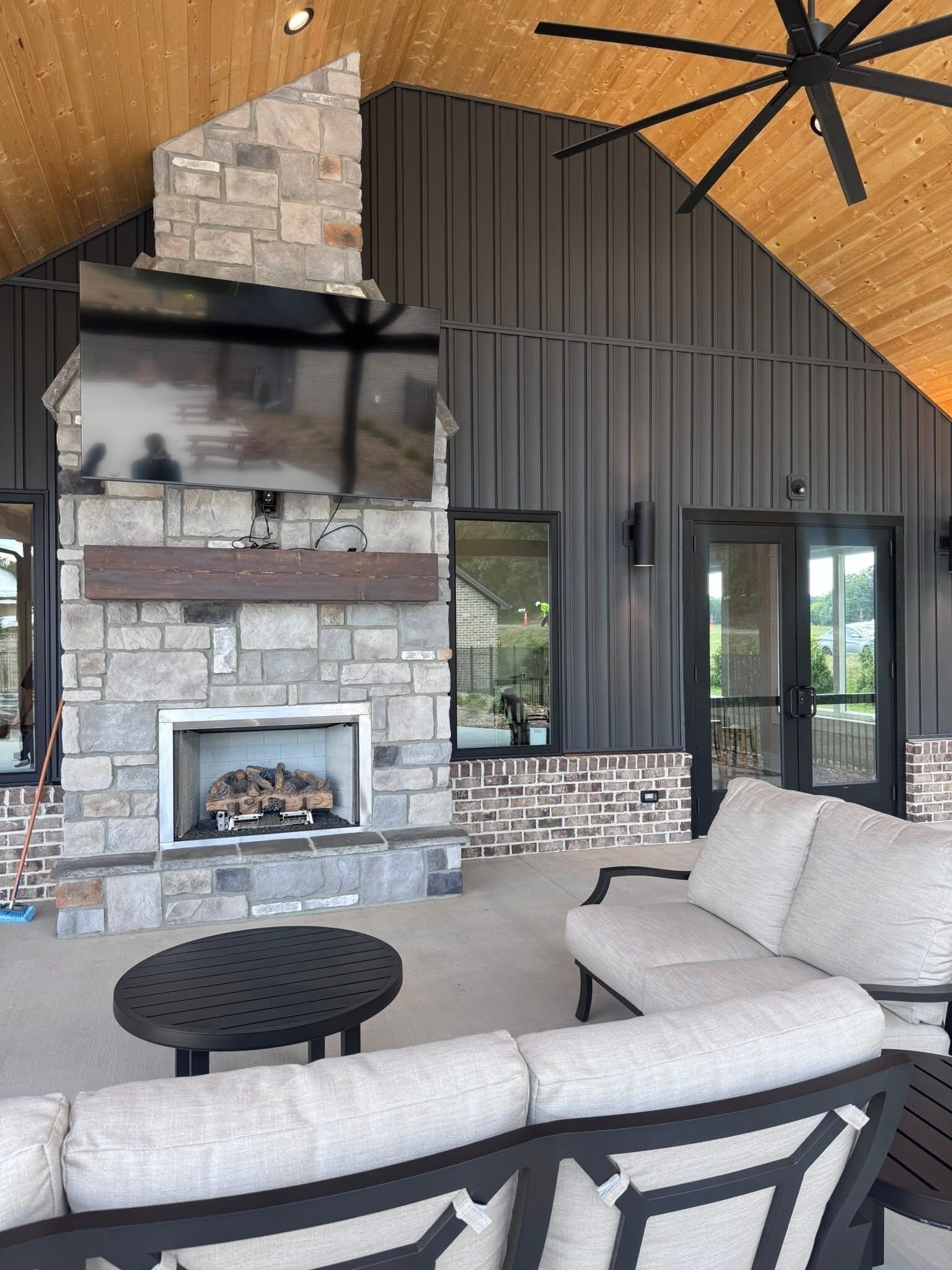 A modern outdoor living space with a stone fireplace, a round table, and a sofa.