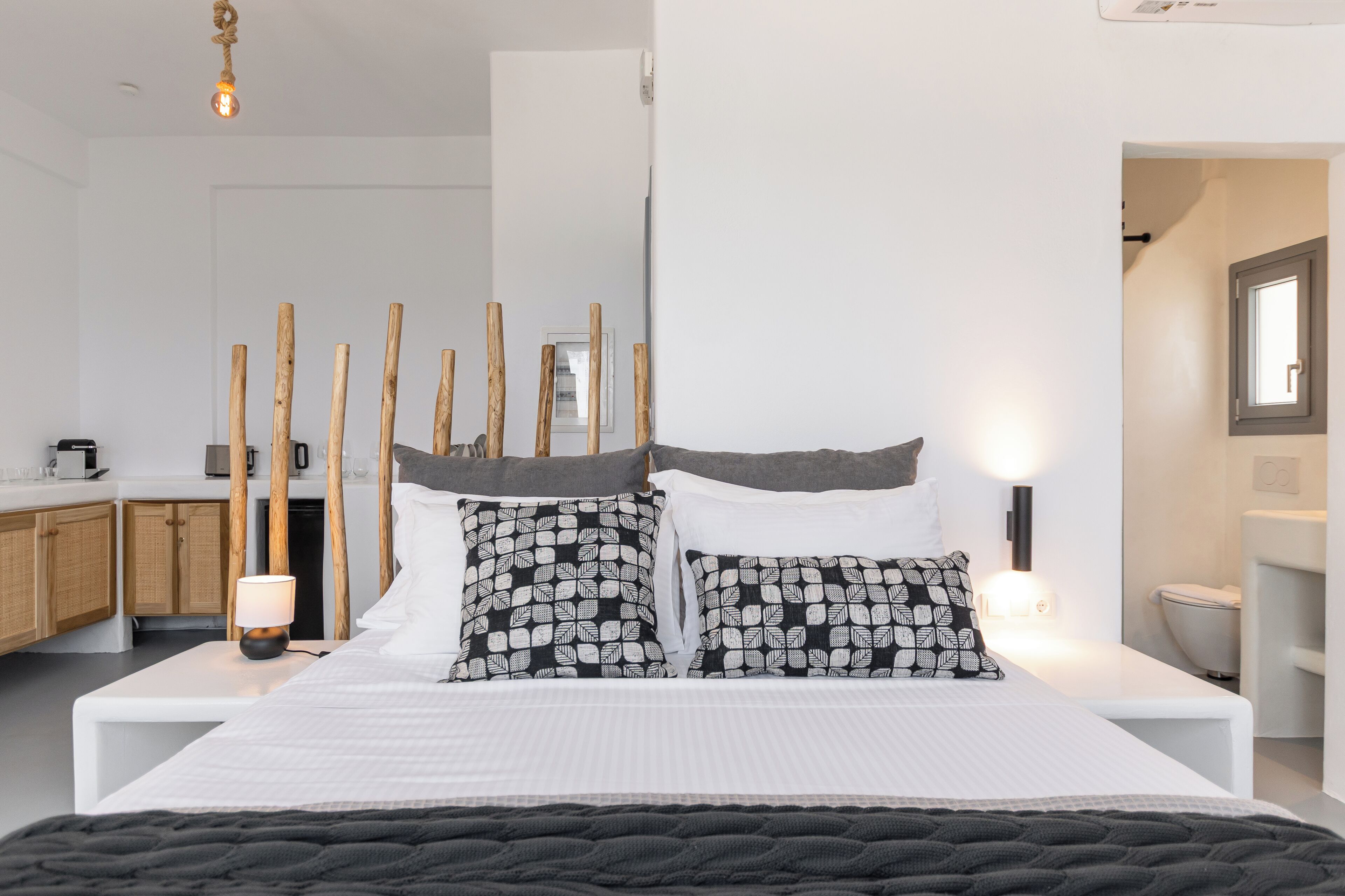 A modern bedroom with a large bed, bedside tables, a nightstand, a lamp, and a mirror.