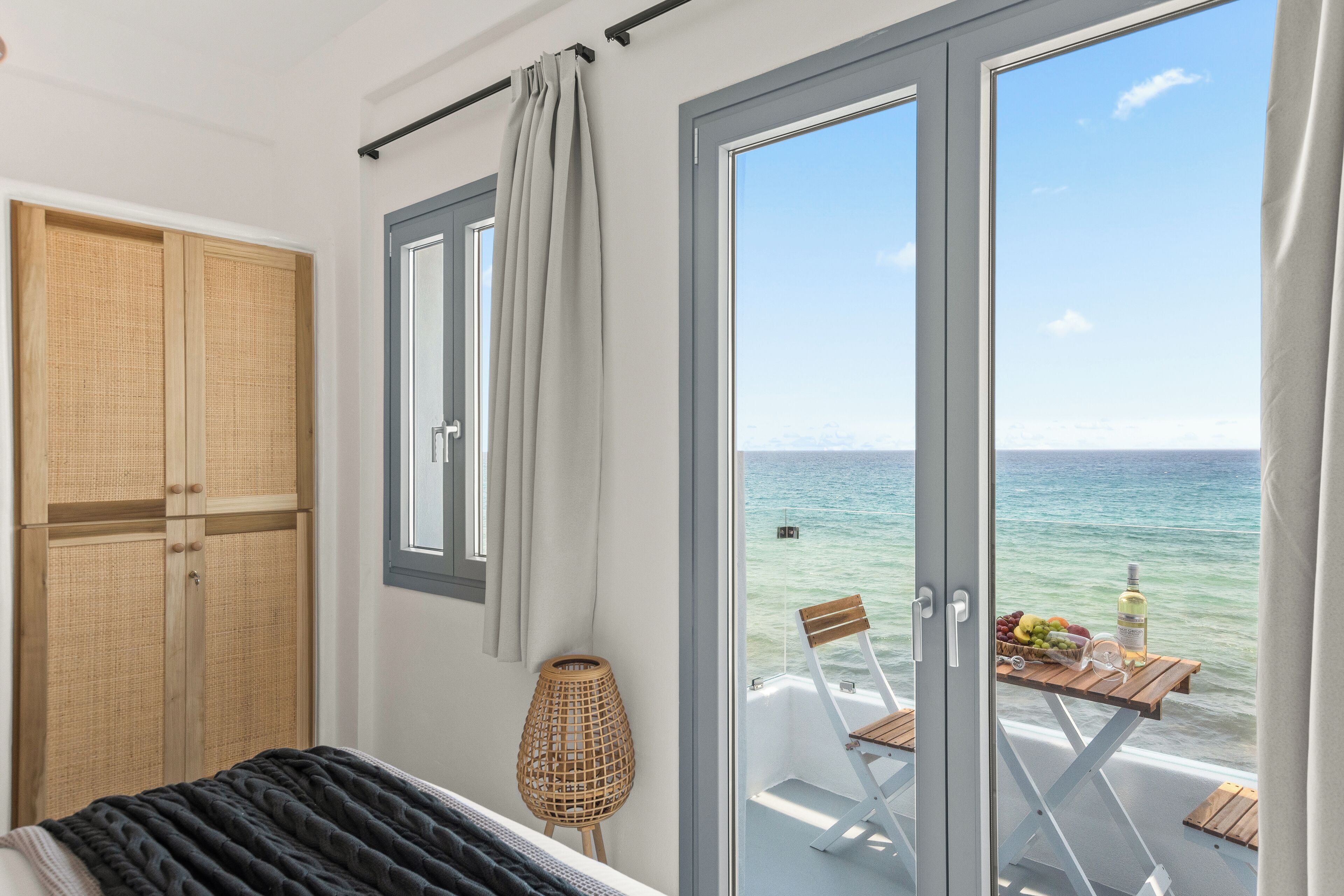 A bedroom with a bed, a wardrobe, a window with curtains, and a view of the sea through a glass door.