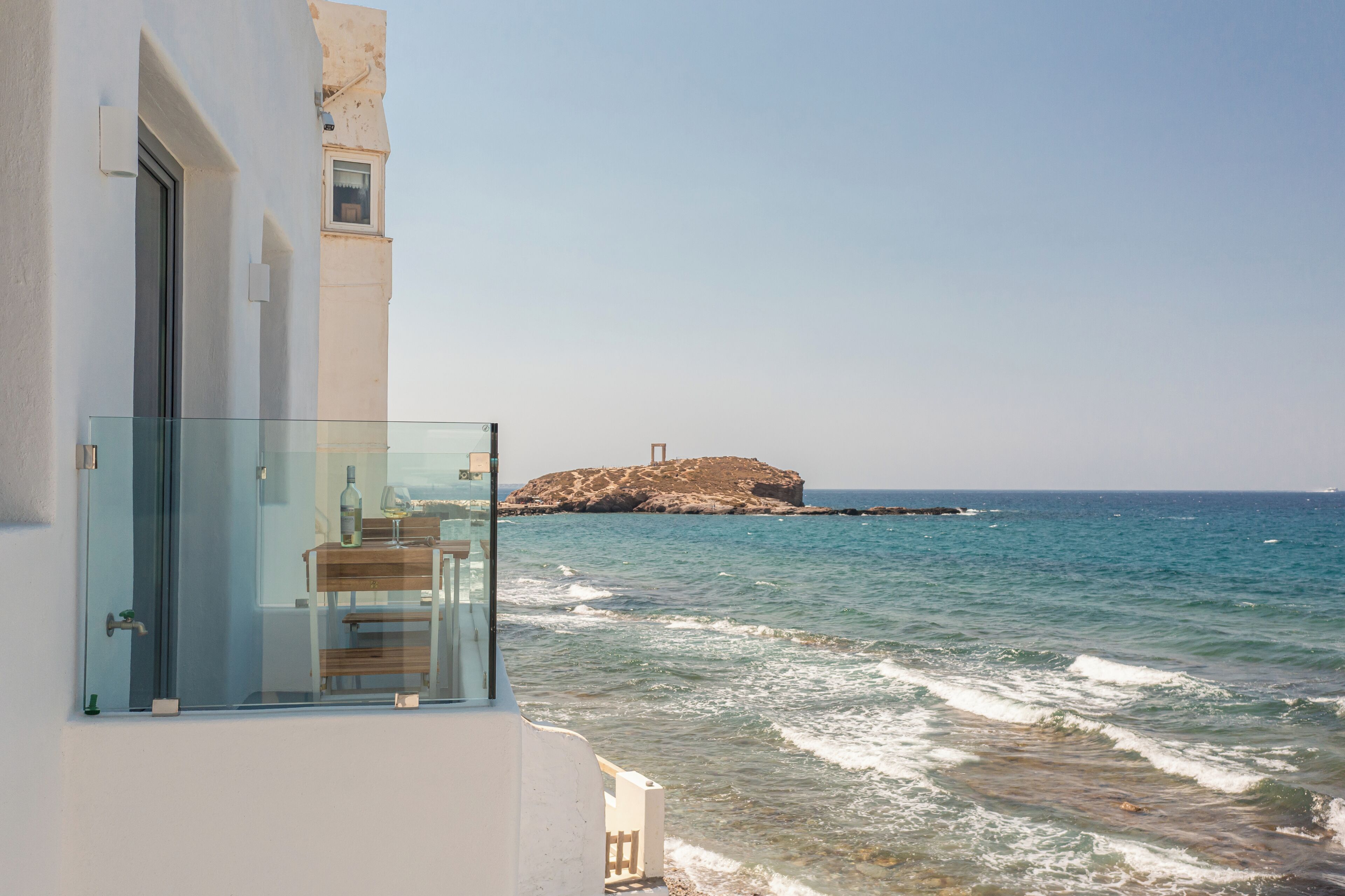 A balcony with a glass railing overlooking a coastal view with a rocky outcrop in the distance.