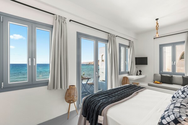 Habitación de hotel con cama, zona de estar, televisión y vista al mar.