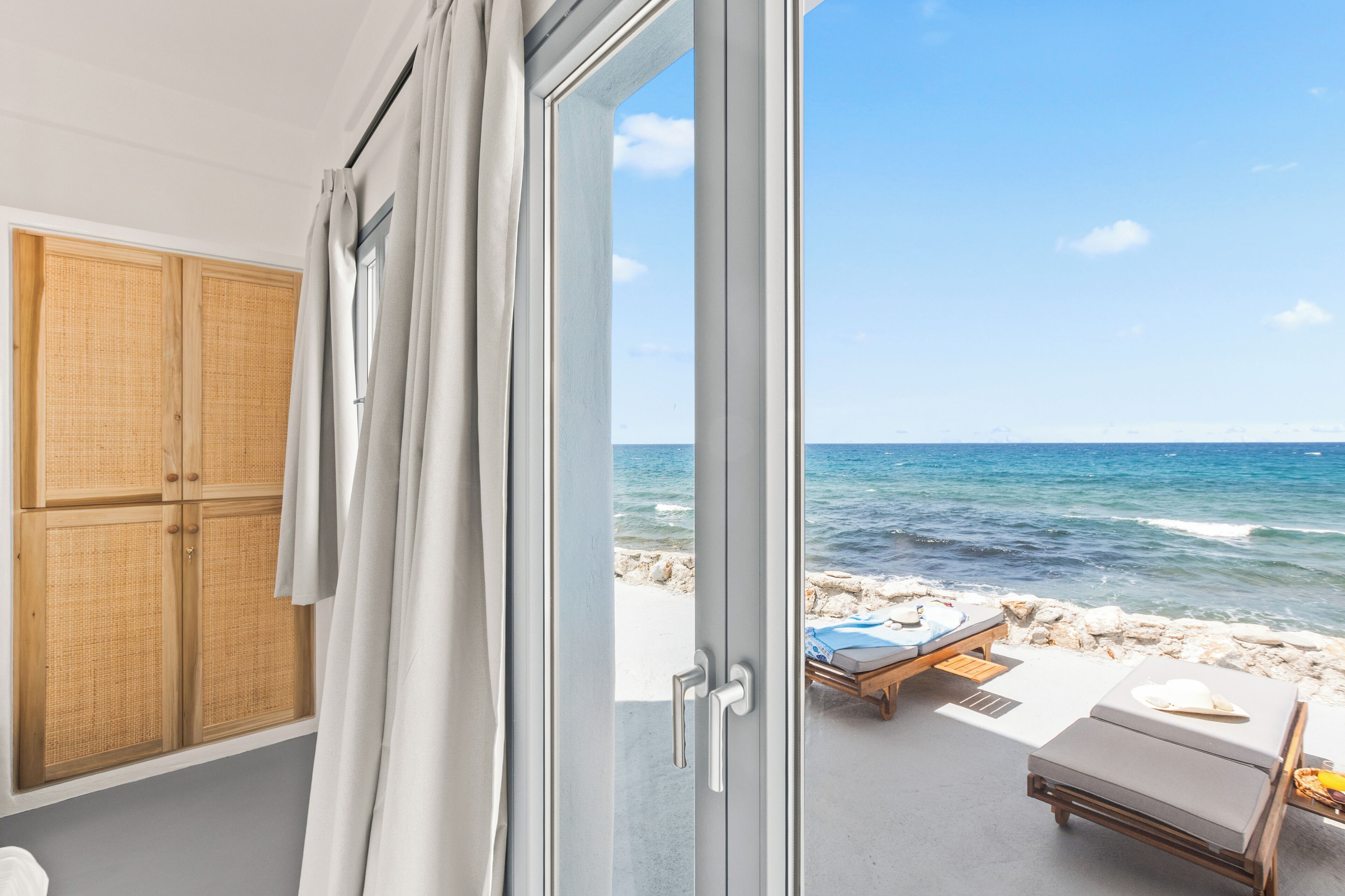 A room with a view of the sea, a wooden wardrobe, and a beachside lounge area.