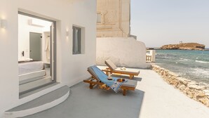 Een hotelkamer aan de kust met balkon en uitzicht op zee, een bed en een klein tafeltje met fruit.