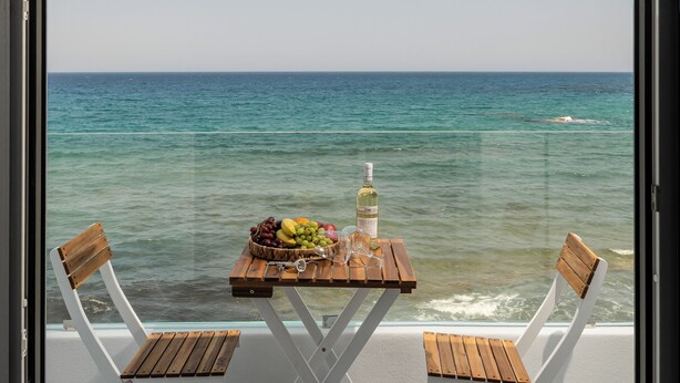 Een tafel met een fles, glazen en fruit op een balkon met uitzicht op zee.