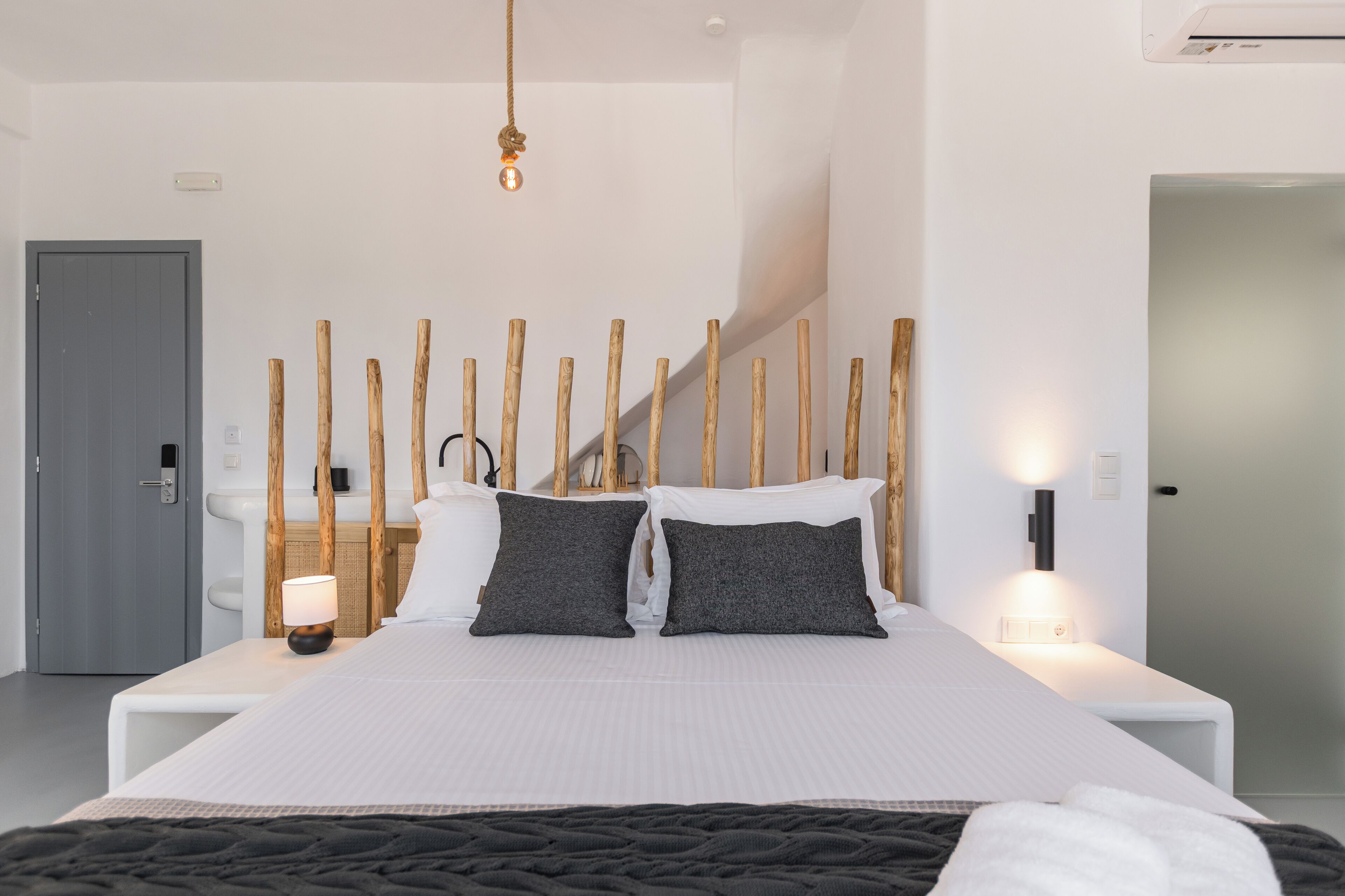 A modern hotel room with a large bed, a wooden headboard, and a view of the staircase.