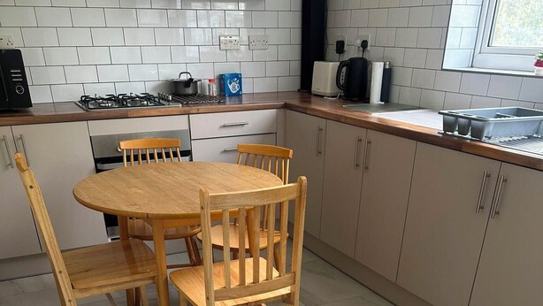 Una cocina con una mesa redonda de madera y sillas, salpicadero de azulejos blancos y armarios grises.