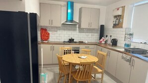 Una cocina compacta con una mesa redonda de comedor, sillas de madera, un refrigerador negro y una campana extractora azul.
