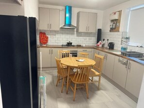 Eine kleine Küche mit einem runden Esstisch, Holzstühlen, einem schwarzen Kühlschrank und einer blauen Dunstabzugshaube.