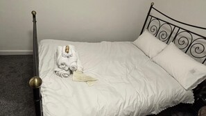 Een bed met een metalen frame, witte beddengoed en een opgerolde handdoek.