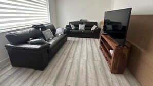 Una sala de estar con un sofá modular, un televisor de pantalla plana y un mueble de entretenimiento de madera.