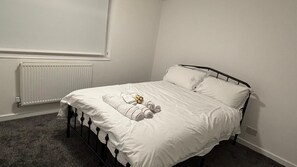 Ein Einzelbett mit weißer Decke und Kissen, ein Heizkörper darunter und eine schlichte Wand.