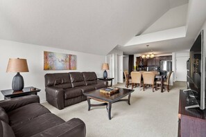 Ein modernes Wohnzimmer mit einer Couch, einem Couchtisch und Lampen. Im Hintergrund befindet sich ein Essbereich mit Stühlen und eine Küche.