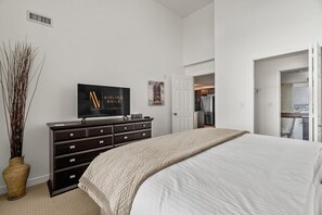 Ein Schlafzimmer mit Bett, Kommode, Fernseher und einer Topfpflanze.