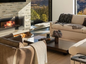 Ein modernes Wohnzimmer mit Kamin, einer Couch, einem Couchtisch und Blick ins Freie.