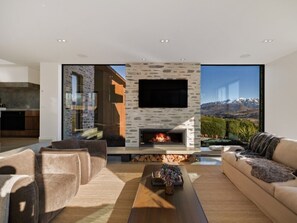 A modern living room with a stone fireplace, a sofa, and a coffee table. - Noa By The Lake | 5 bedrooms, lake view, spa pool, outdoor fireplace (Lake Hayes Estate)