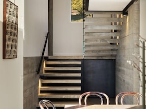 Eine Treppe mit modernem Design, ein Essbereich mit Stühlen und ein gerahmtes Kunstwerk an der Wand.