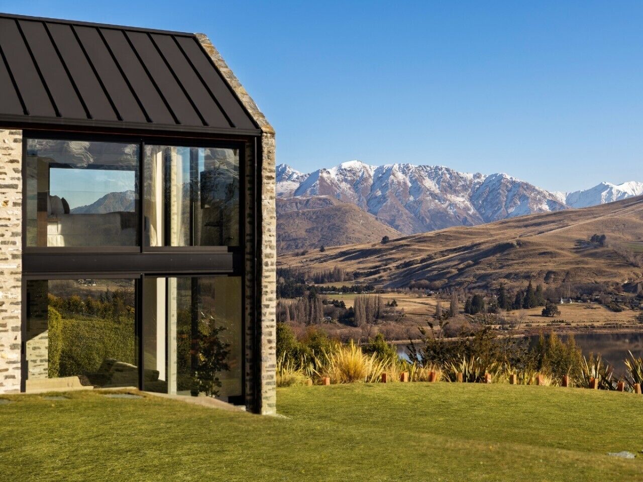 A modern house with large windows, a stone facade, and a view of snow-capped mountains.