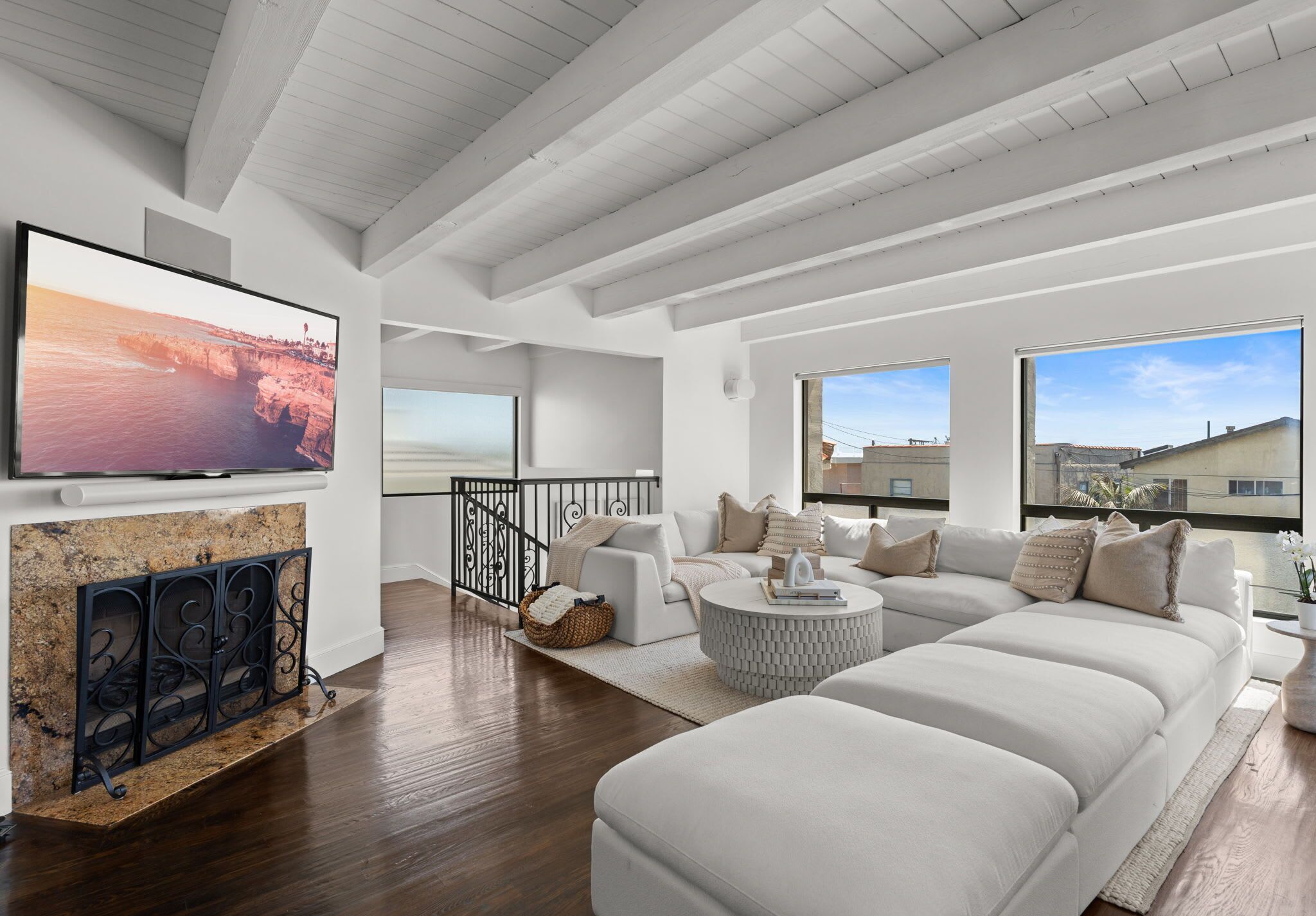 A modern living room with a fireplace, a large flat-screen TV, a sofa set, and a balcony with a view.