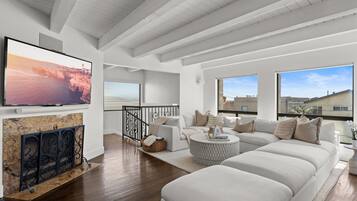 A modern living room with a fireplace, a large flat-screen TV, a sofa set, and a balcony with a view.