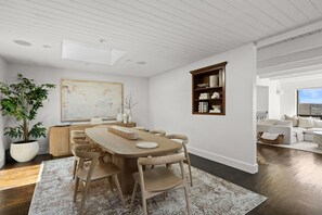 Ein moderner Essbereich mit einem Holztisch und Stühlen, einer großen Kühlpflanze und einer weißen Wand mit Regal.