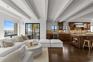 Ein modernes Wohnzimmer mit Ecksofa, einem Essbereich und einer dahinterliegenden Küche, sowie Blick ins Freie.