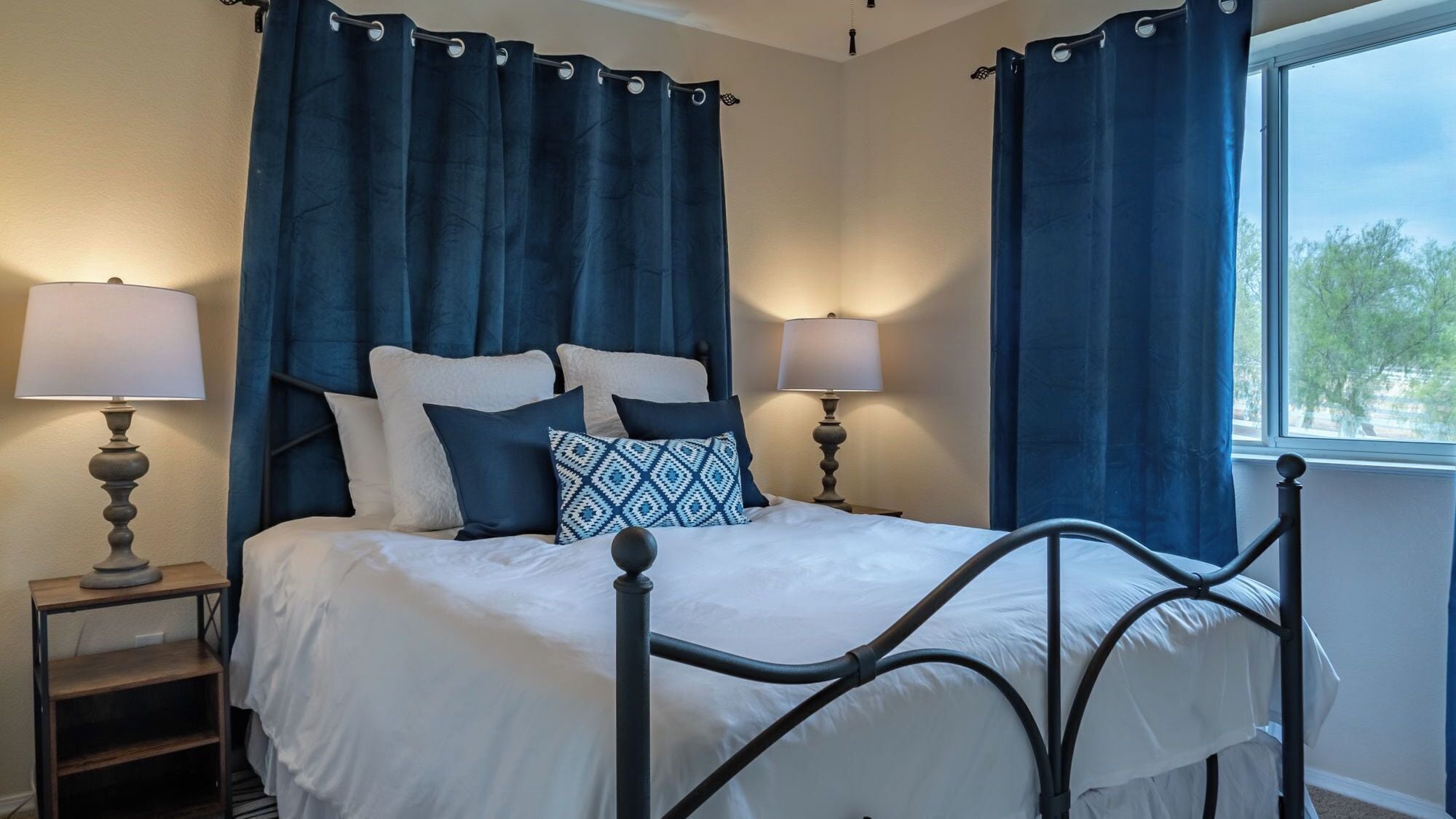 A bedroom with a four-poster bed, two bedside tables with lamps, and a view of the outdoors through a window.