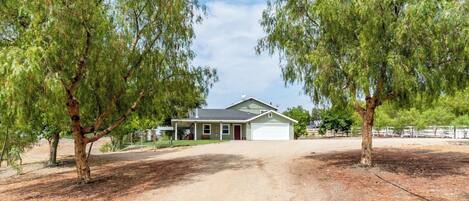 A single-story house with a garage, surrounded by trees, and a gravel driveway.