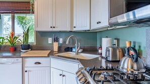 A kitchen with white cabinets, a stainless steel range hood, a gas stove, a sink with a modern faucet, and various kitchen items on the countertop. - Sunset at Nirvana by Avantstay Pool + Hot Tub + Games Paso Robles Wine Country (San Miguel)