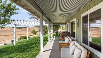 Un portico coperto con un'area salotto, vista su un paesaggio collinare e una struttura a pergola.