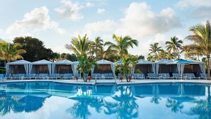 Ein Swimmingpool mit Liegestühlen und Sonnenschirmen, umgeben von Palmen.