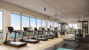 Ein Fitnessstudio mit Laufbändern, Hanteln und Trainingsgeräten, großen Fenstern und Meerblick.