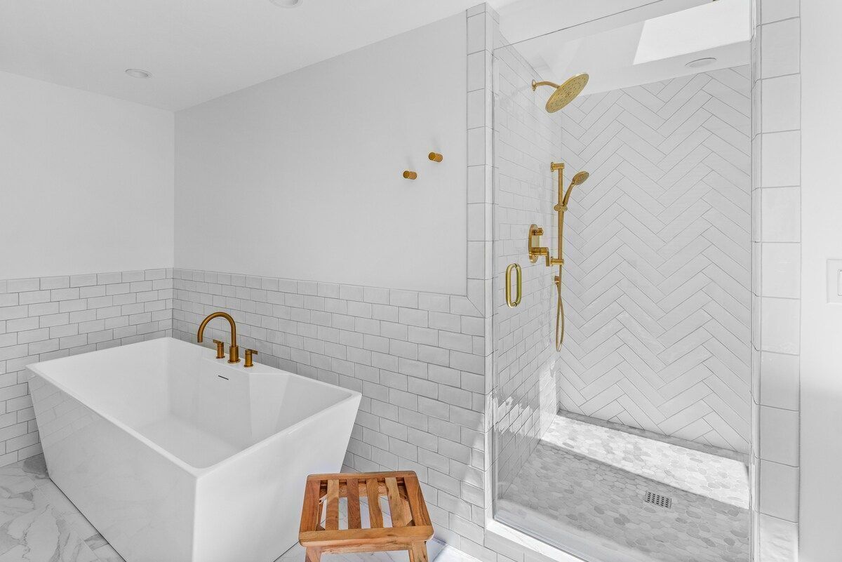 Un baño moderno con una bañera independiente, ducha con mampara de vidrio y un taburete de madera.