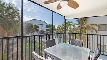 Ein Balkon mit Glastisch und Korbstühlen, der auf einen Wohnbereich mit Palmen und einem Haus blickt.
