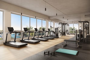 Un gimnasio con cintas de correr, mancuernas y equipo de ejercicio, ventanas amplias y vistas al exterior.