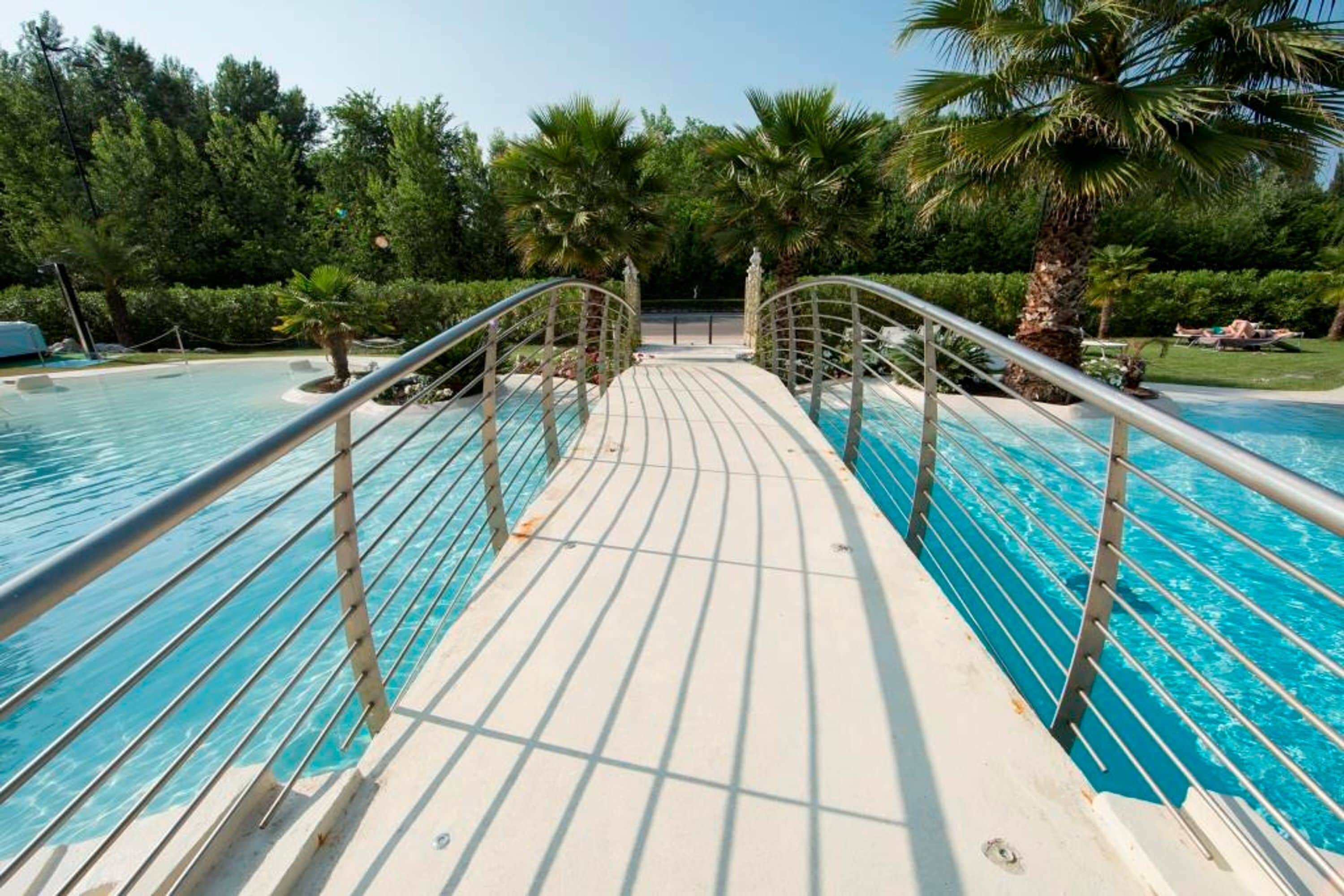 Ein Poolbereich mit einer Promenade, Palmen und blauem Himmel.
