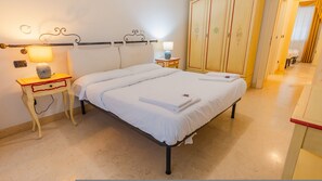 Ein Doppelbett mit weißer Bettwäsche, ein Nachttisch mit Lampe und ein Schrank mit floralem Dekor.