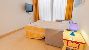 Et hotelværelse med en seng, et sengebord med lampe, et fjernsyn ophængt på væggen og et vindue med gardiner.
