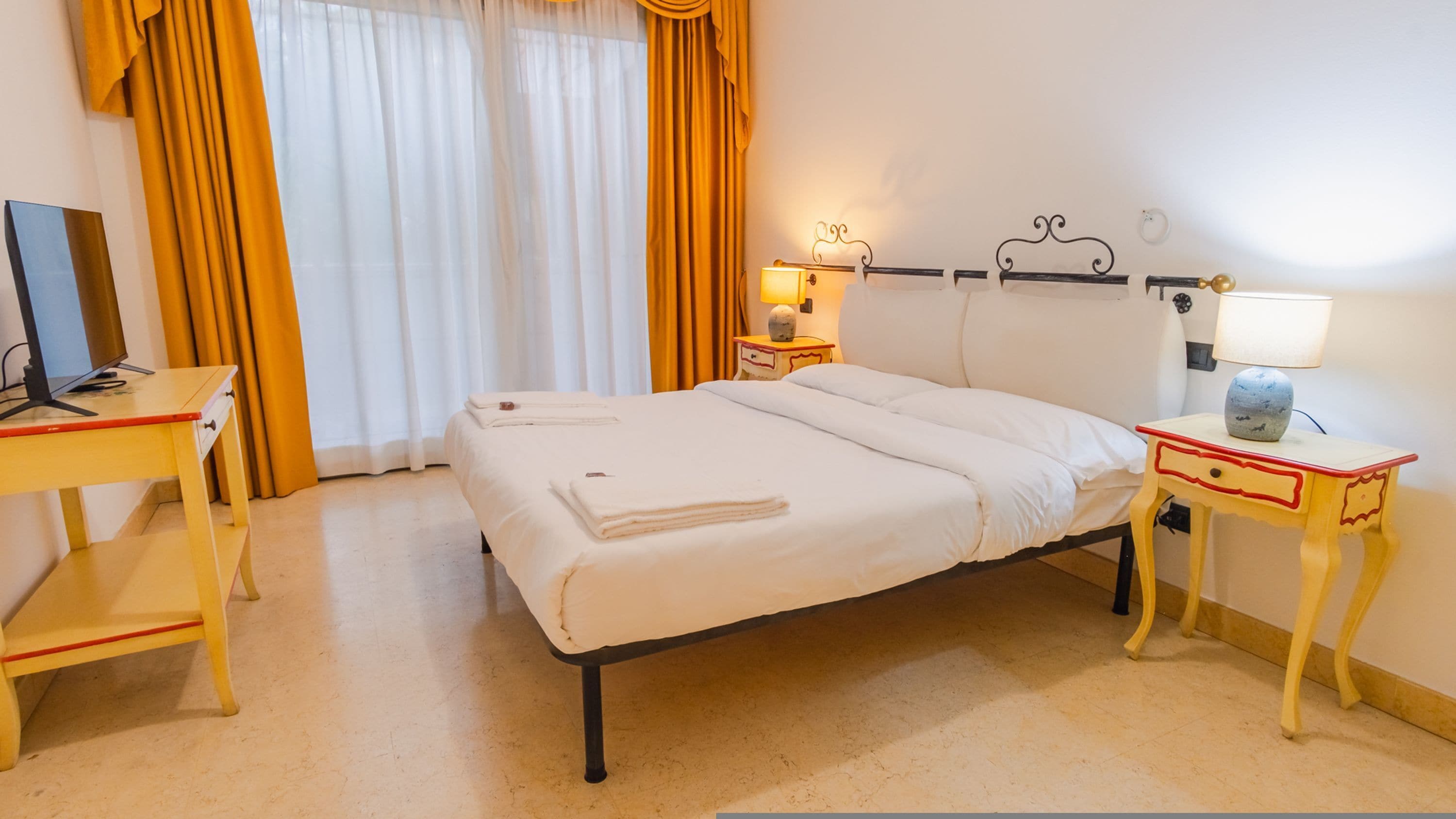 A hotel room with a bed, bedside tables, a desk, and a lamp.