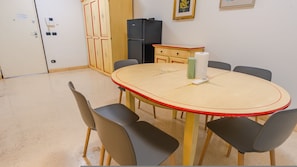Ein Konferenzraum mit rundem Tisch, sechs Stühlen, einem Kühlschrank, einem Schrank und einem an der Wand befestigten Thermostat.