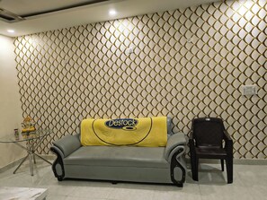 Ein Zimmer mit Wandverkleidung, ein Sofa mit gelber Decke, ein Sessel und ein kleiner Tisch mit Glasplatte.