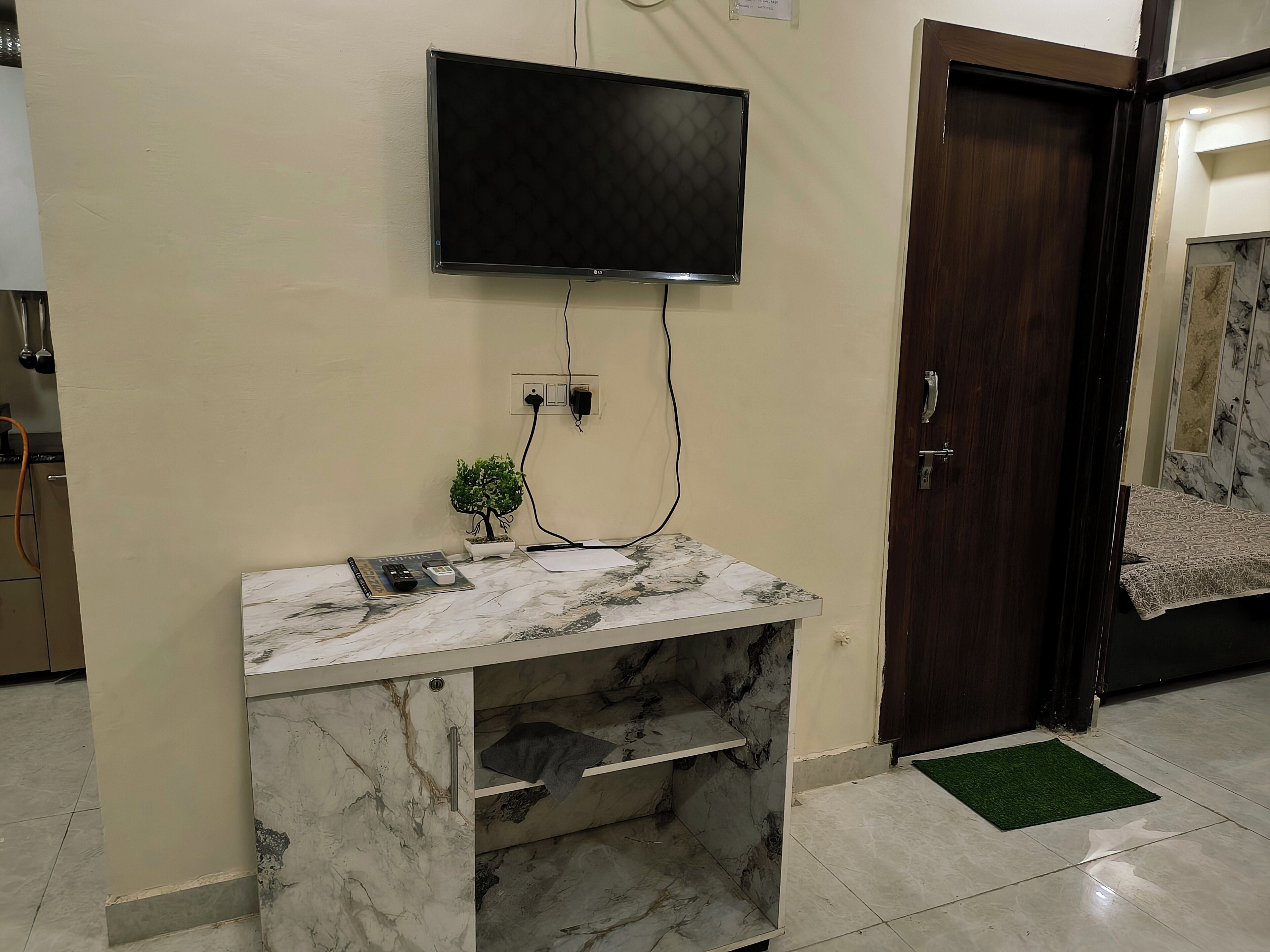 Une pièce avec une console en marbre, un téléviseur fixé au mur, une petite plante en pot et une porte en bois.
