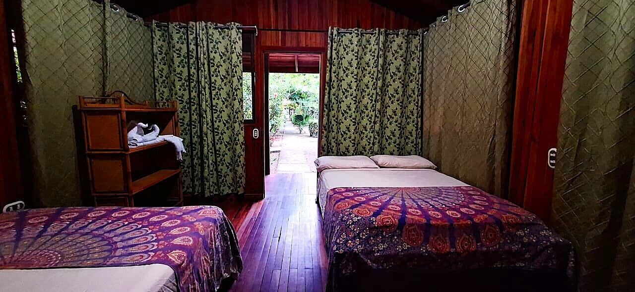 Una habitación con dos camas, un banco de madera y una puerta que da al exterior.