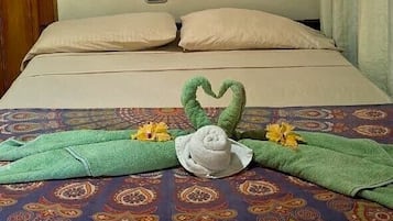 Een bed met een bedspreider met een patroon, een hartvormige decoratie op het bed, en een luchtverkoeler aan de muur.