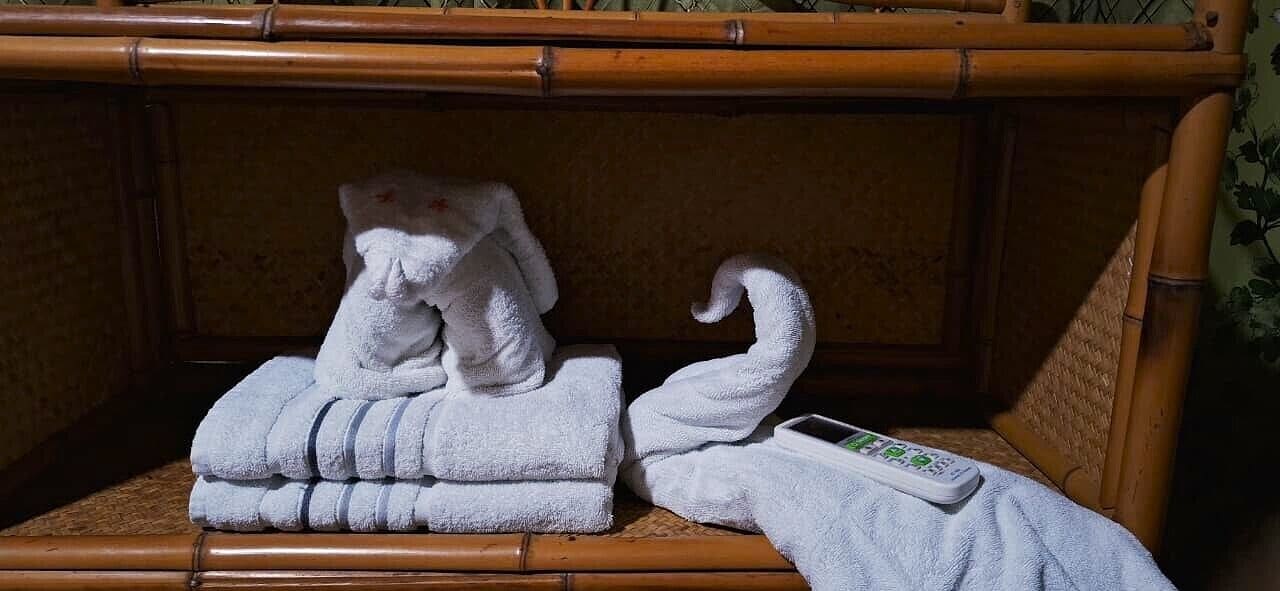 Una habitación con cabecera de bambú, una toalla doblada y un control remoto sobre una superficie de madera.