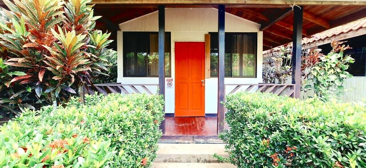 Un edificio con puerta roja, rodeado de abundante vegetación.