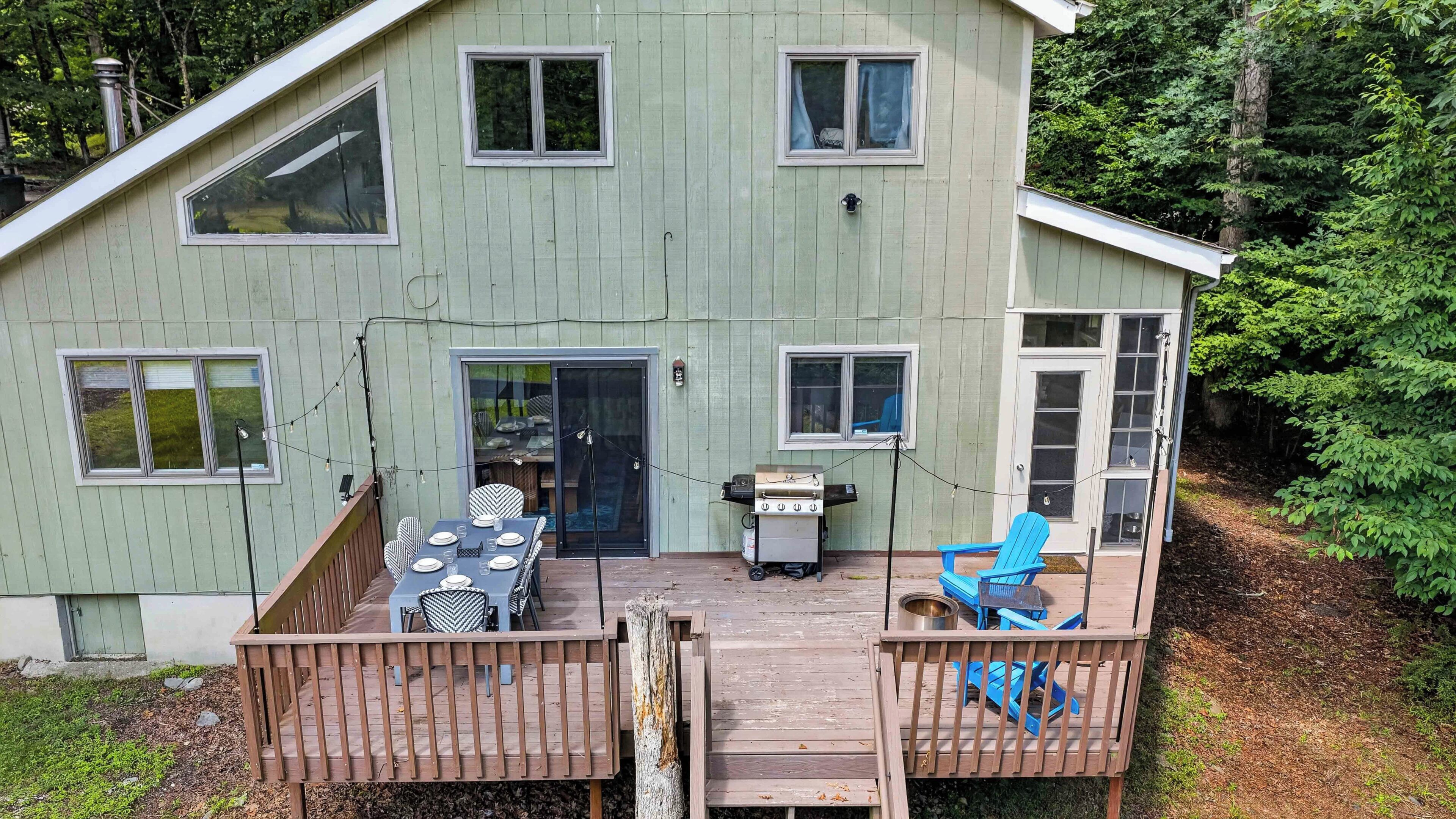 A two-story house with a deck, a grill, and a blue chair.