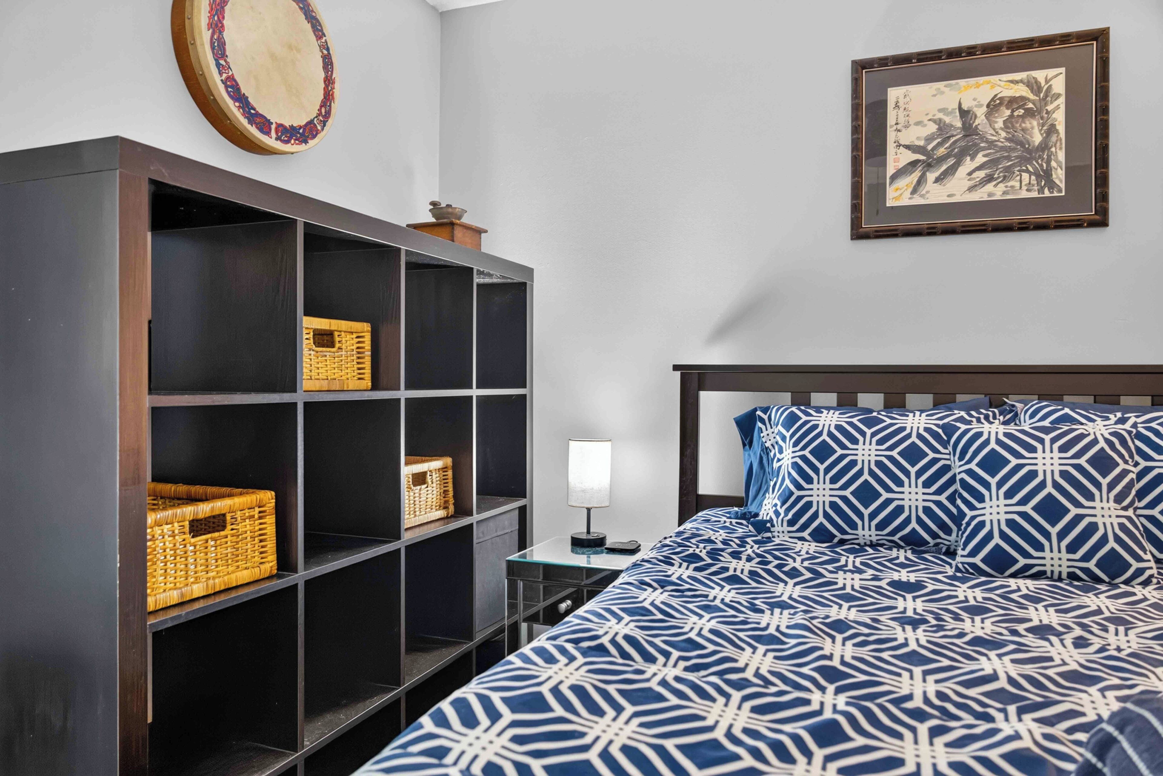 A bedroom with a bed, a nightstand, a wall-mounted shelf with baskets, and a framed picture.