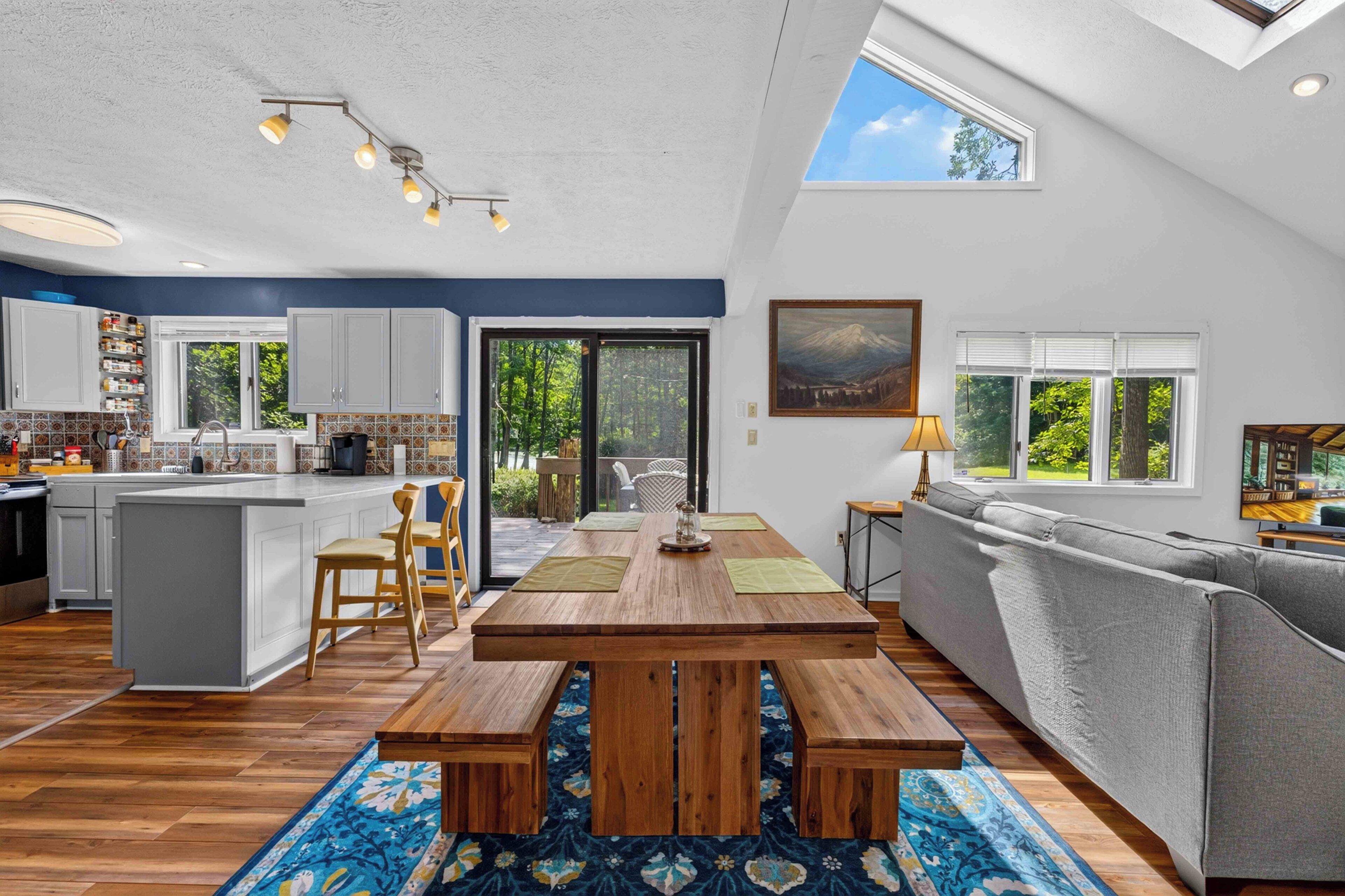 A spacious kitchen with a central island, a dining area with a wooden table, and a living room with a sofa and a TV.