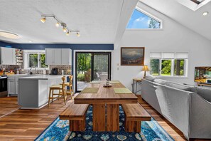 Una cocina amplia con una isla central, un comedor con una mesa de madera, y una sala de estar con sofá y televisor.